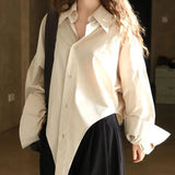 A woman wearing an oversized shirt blouse with an irregular hem, in a beige color, paired with a dark skirt.