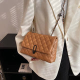 A tan quilted leather shoulder bag with a black metal clasp and a brown-and-black chain strap, worn by a person in a white blazer.