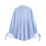 A blue and white vertically striped long-sleeve blouse shown from the back, featuring white cuffs and blue-and-white striped tie details at the sleeves, on a solid white background.