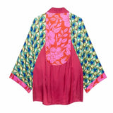 A women's kimono-style robe shown flat against a white background, featuring a solid magenta pink front panel and a back panel with a red-orange floral print, flanked by patterned sleeves in green, blue, and gold.