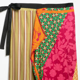 A multicolor patchwork skirt with distinct panels including vertical stripes in olive and beige, a green geometric pattern, a bright orange floral section, and a bold pink floral print, finished with a black waistband and tie.