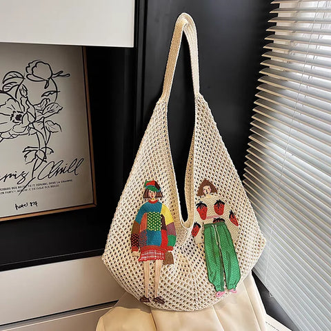 Mesh bag with embroidered designs of people and fruit on a mannequin against a dark wall.