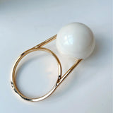 Gold ring handle  with a large white bead clutch bag on a light gray background