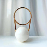 Decorative object handbag with gold circular top and white sphere base on a light background