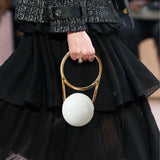 Person holding a gold and white handbag with a black outfit