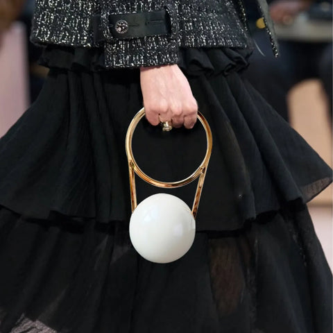 Person holding a gold and white handbag with a black outfit